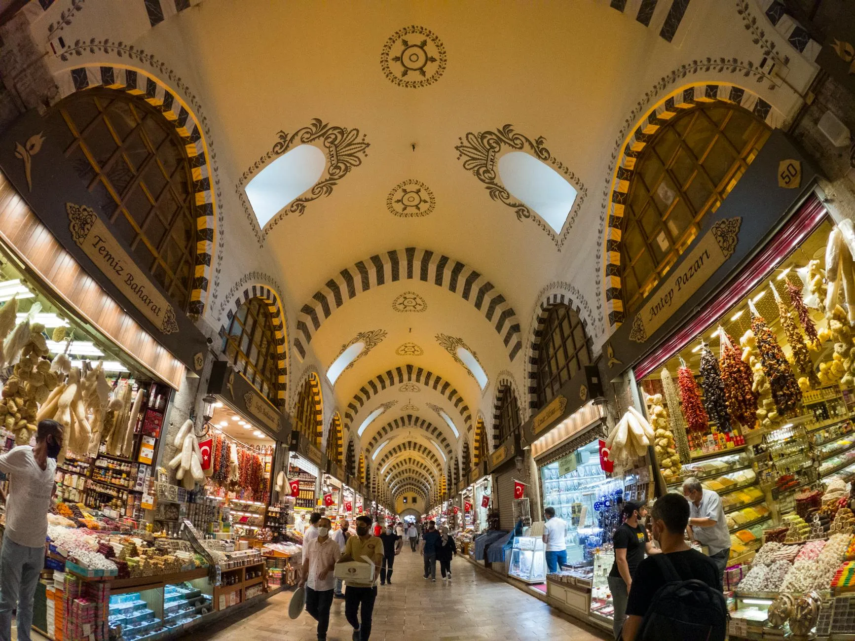 The ornate yellow arched ceilings of Istanbul&#x27;s Grand Bazaar, with shops and Turkish flags below