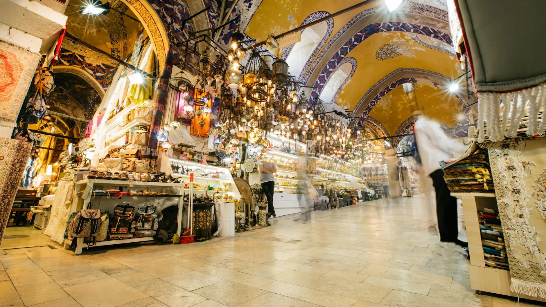 Inside the Grand Bazaar (Kapalıçarşı) in Istanbul, with painted vaulted ceilings, hanging ornamental lamps and jewelry-shop windows along a polished stone aisle
