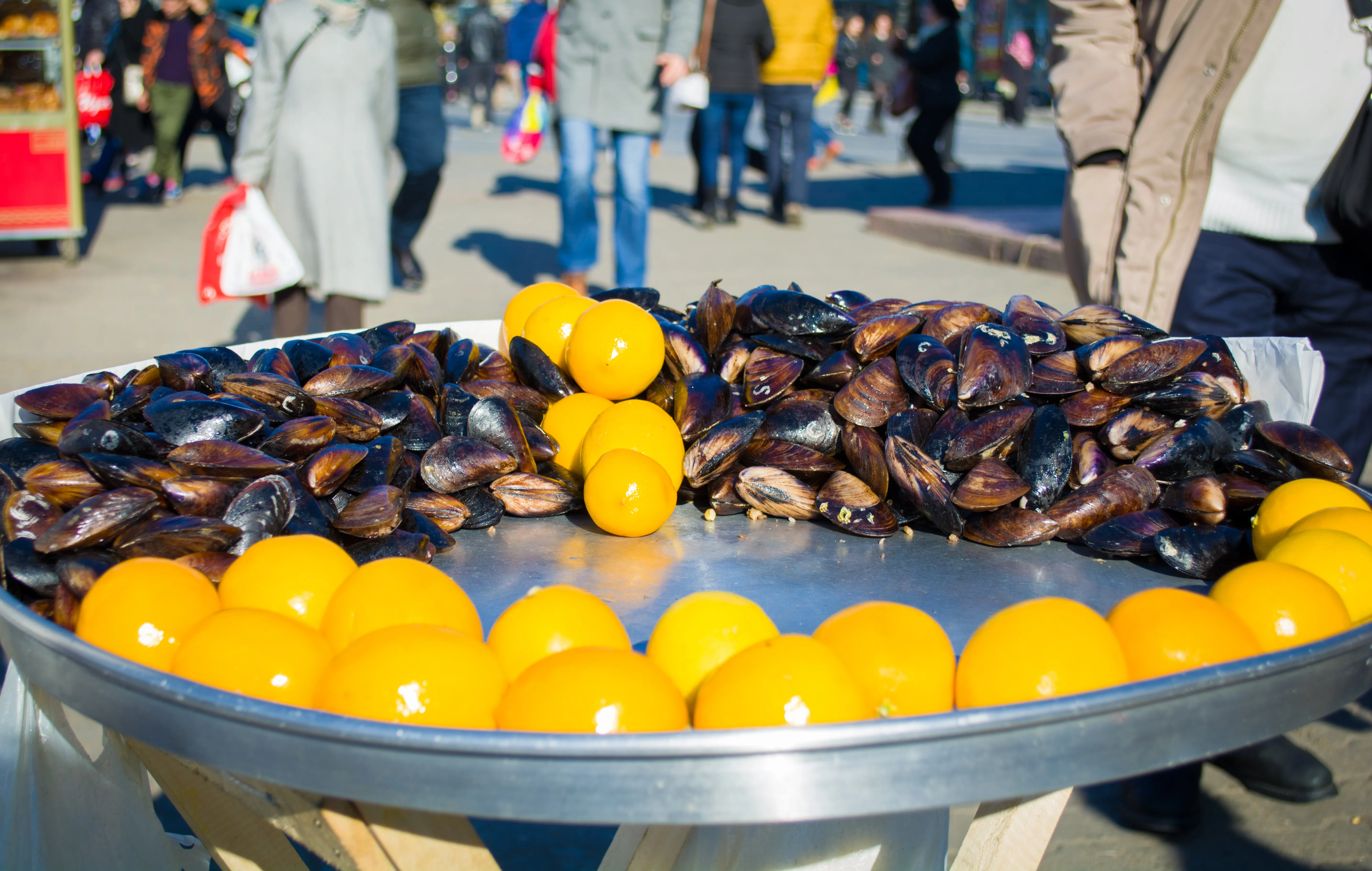 A round metal tray of stuffed mussels (midye dolma) with rows of yellow lemon squeeze-bottles on a Kadıköy street cart