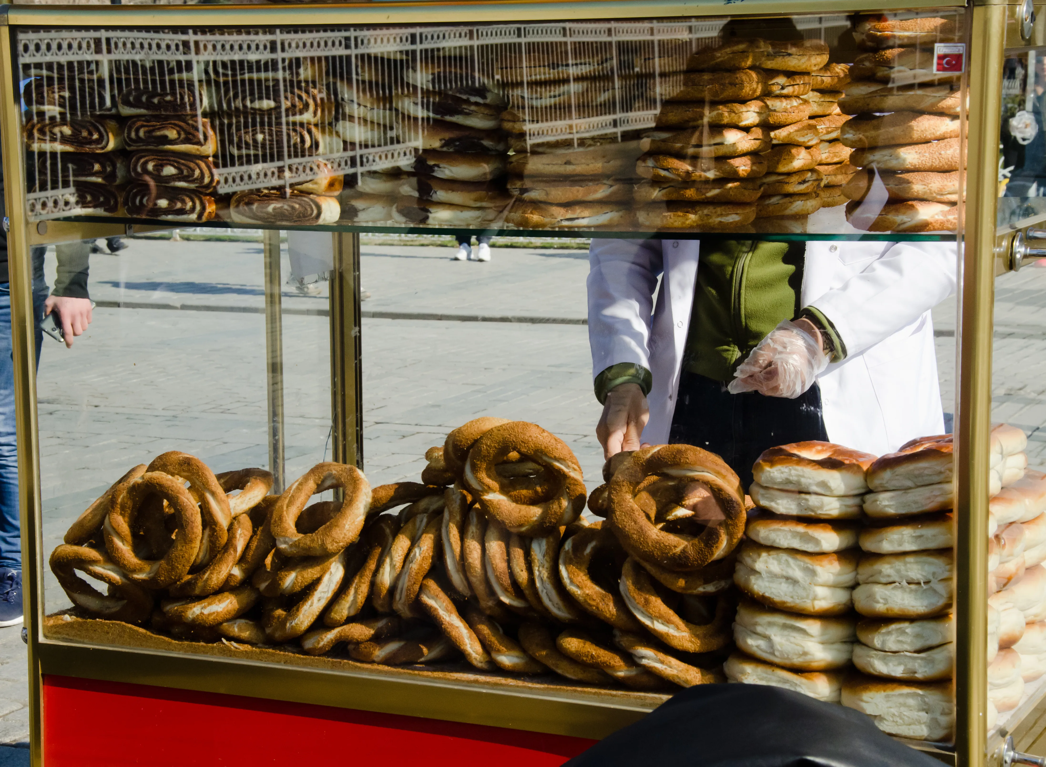 A simit seller behind his traditional red street cart stacked with sesame-covered bread rings in Istanbul