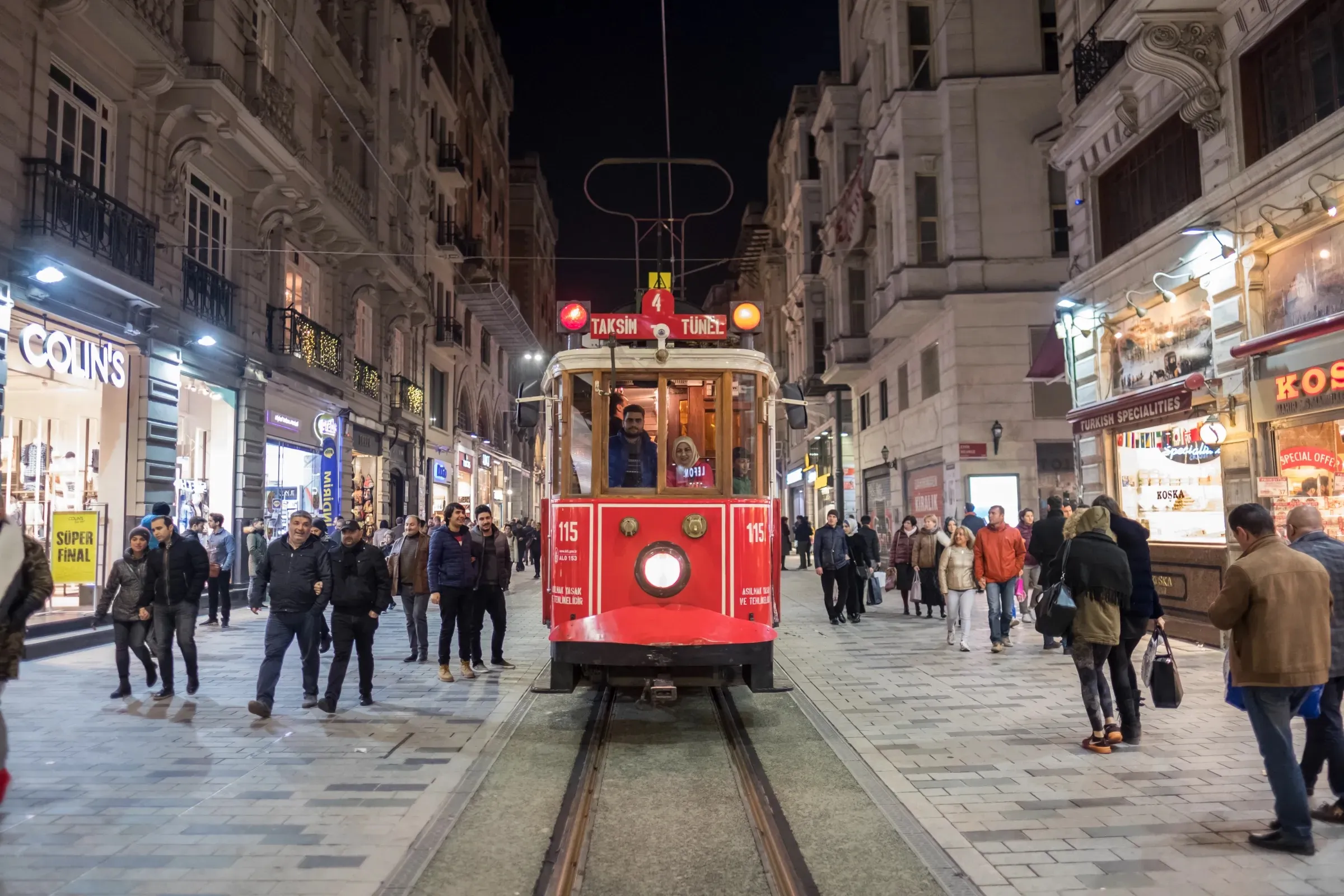 The historic red Taksim-Tünel nostalgic tram on Istiklal Street in the evening, with crowds walking past