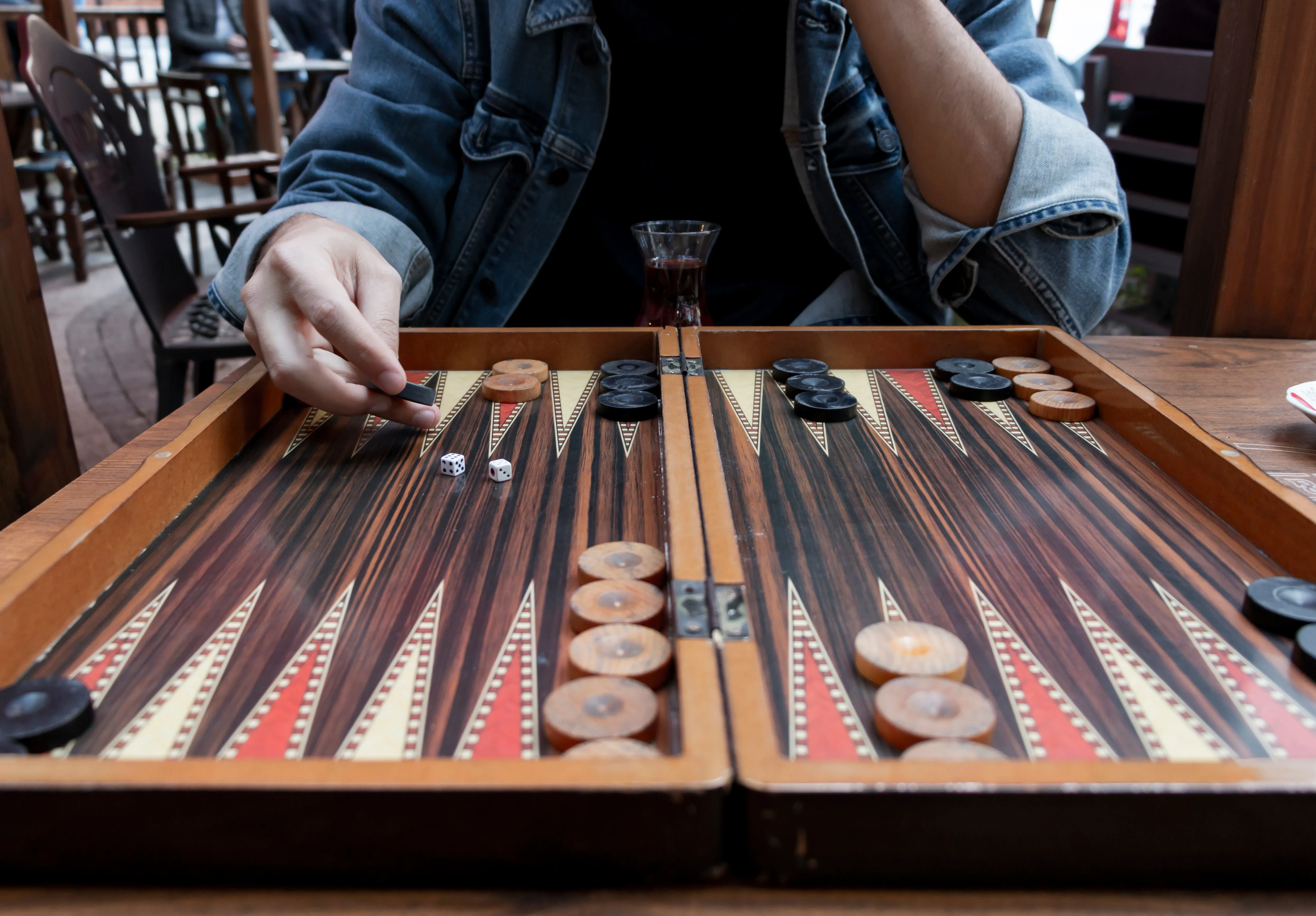 Close-up of a man&#x27;s hand holding a checker over a traditional Turkish tavla (backgammon) board