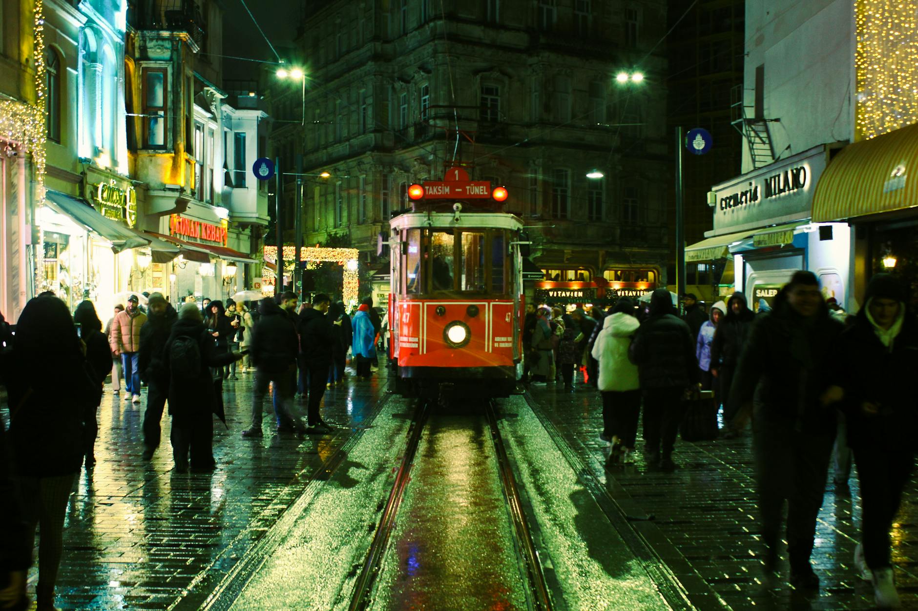 The red nostalgic tram on a rain-slicked İstiklal Caddesi at night, surrounded by crowds