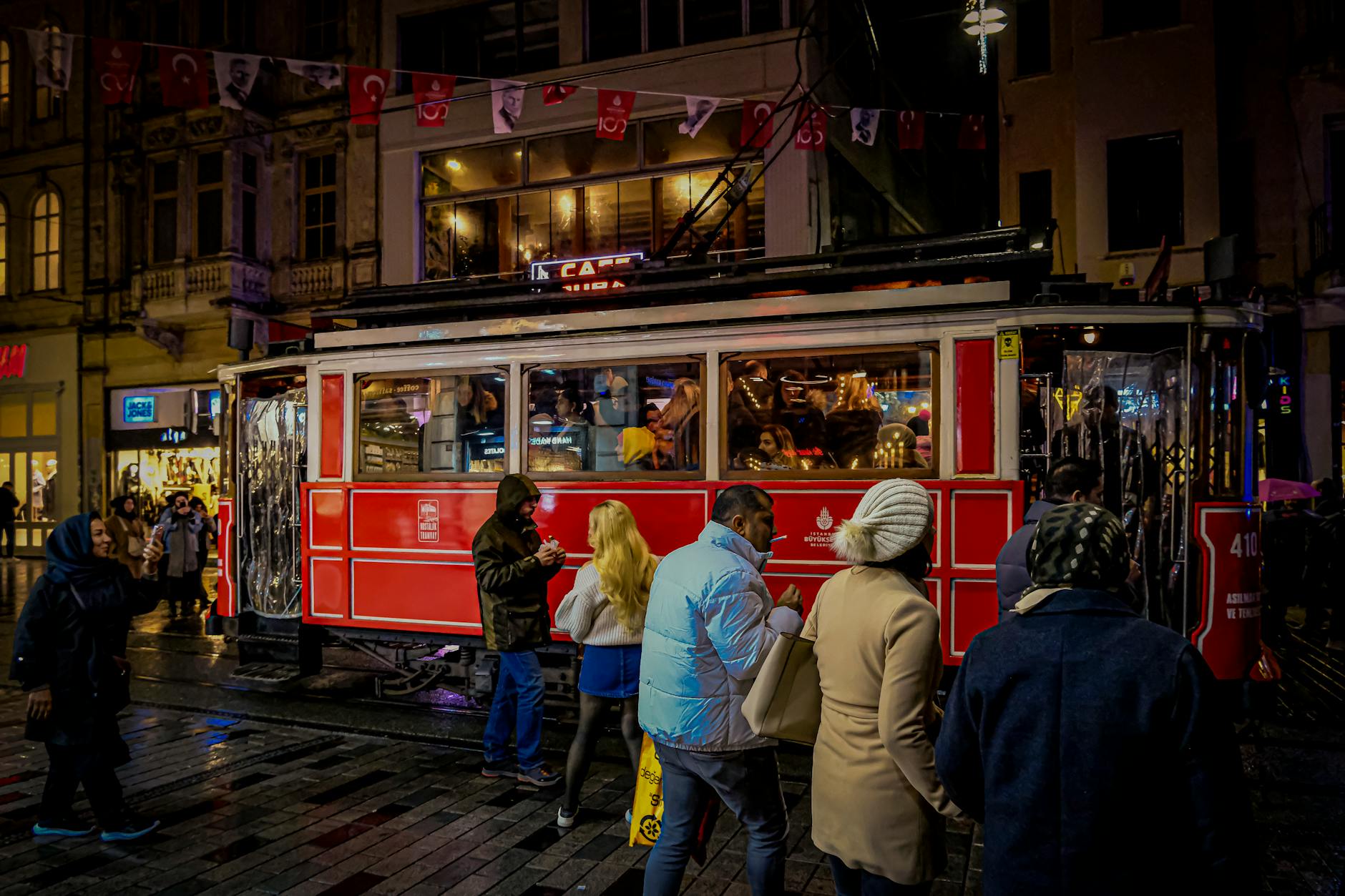 The historic red nostalgic tram on İstiklal Caddesi at night with Turkish flags and pedestrians on the street