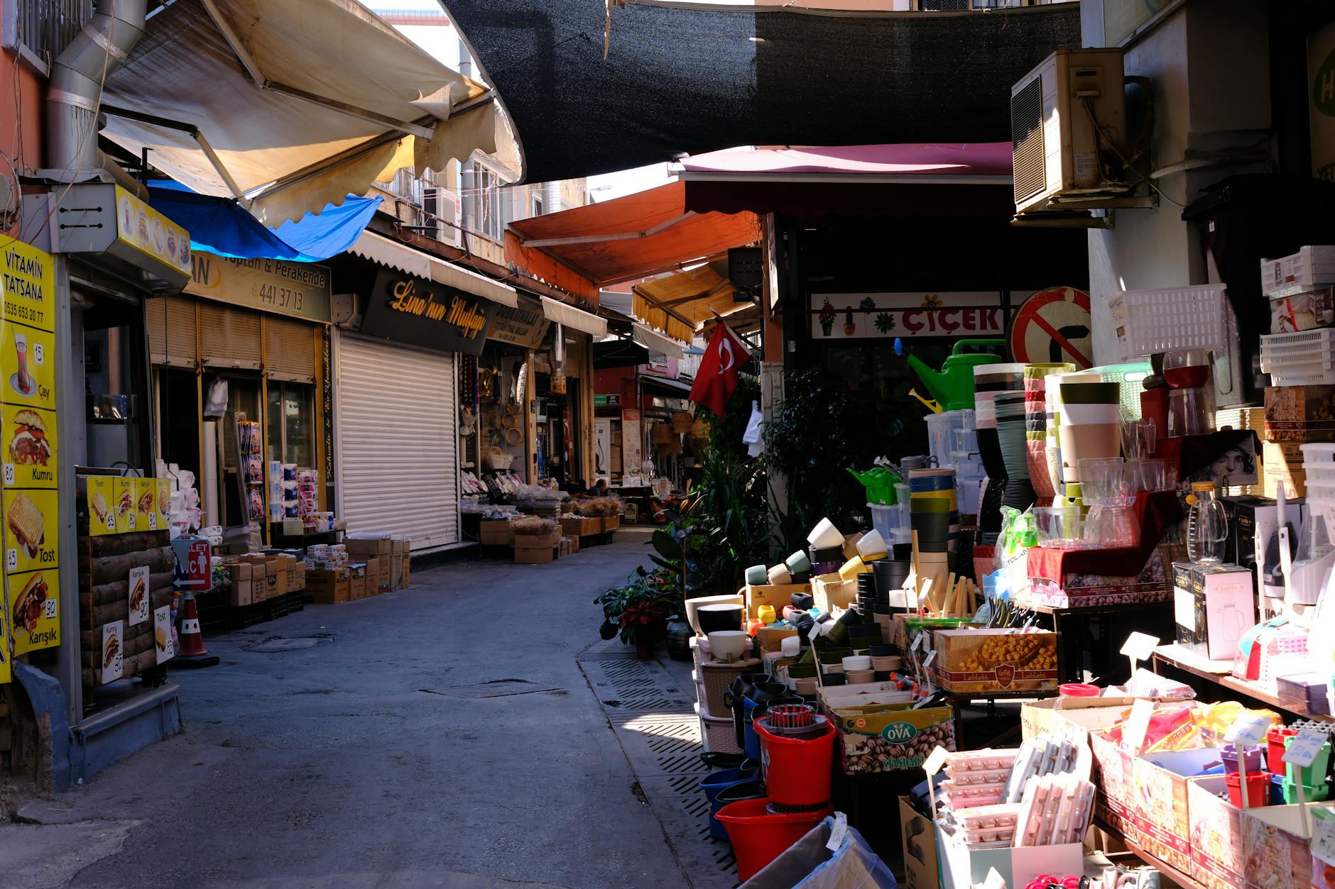 A narrow covered alley in a working-class Istanbul bazaar, lined with small shops selling dry goods and household items