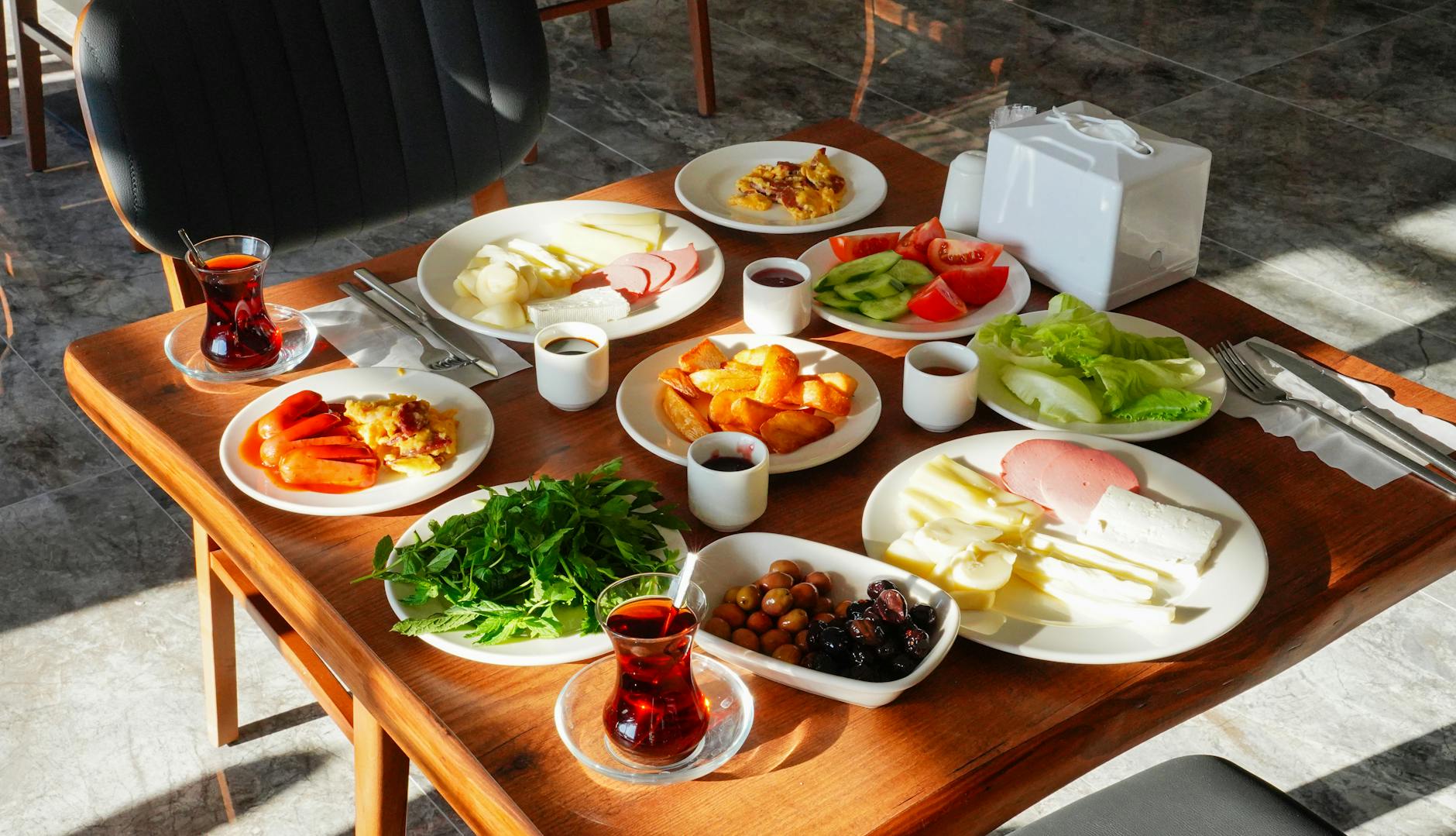 A traditional Turkish breakfast laid out overhead on a wooden table with multiple small plates, olives, cheese, jams and tulip tea glasses