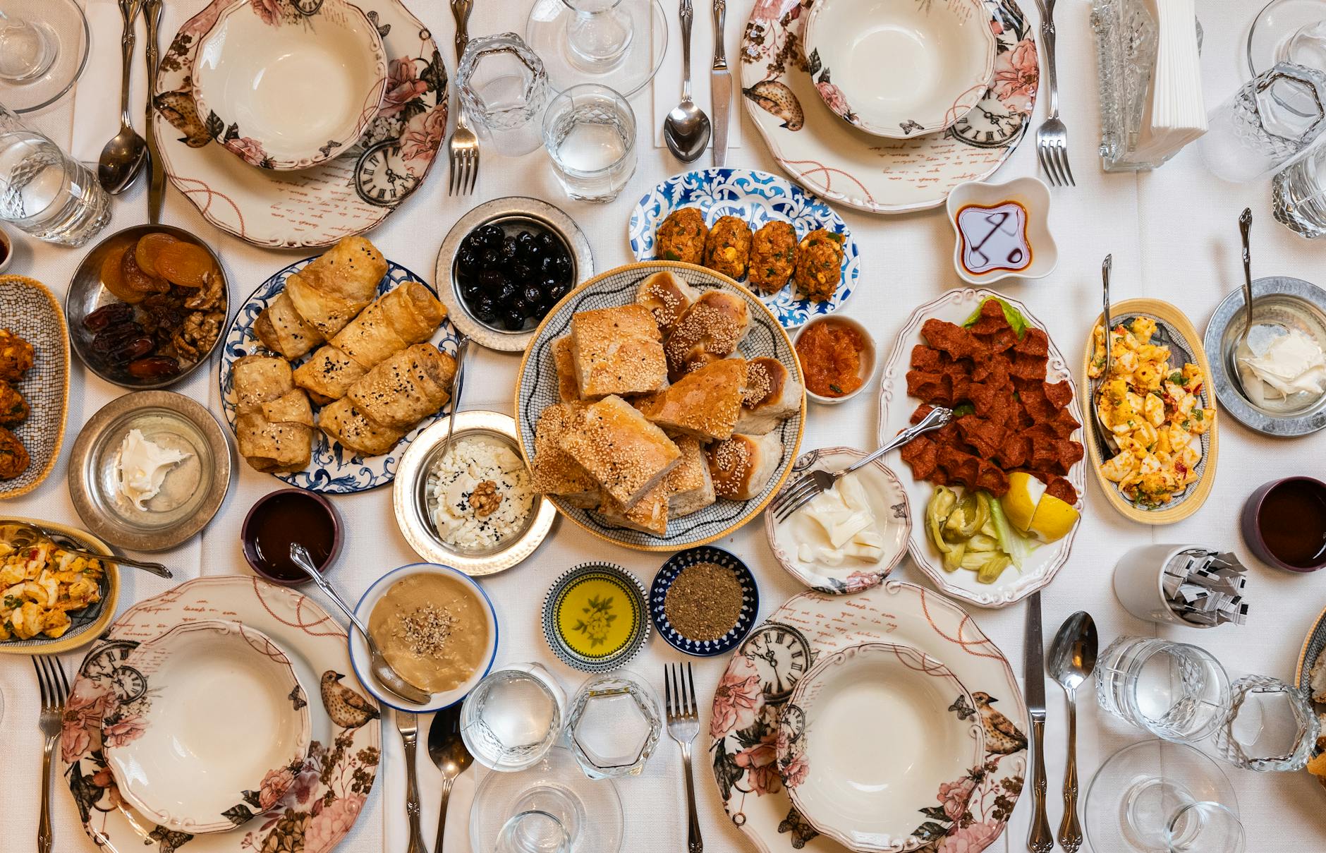 An overhead Turkish feast with olives, bread, dips, meze and small plates covering a floral-printed tablecloth